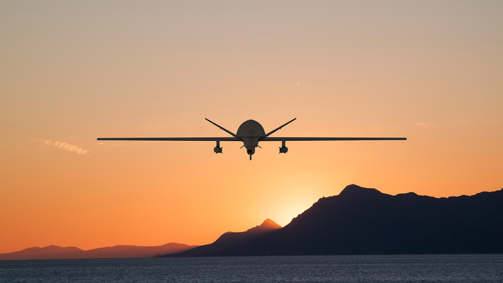 Silhouette of spy drone flying over  sea (UAV) and on background beautiful view of sun hiding behind  surface of mountain